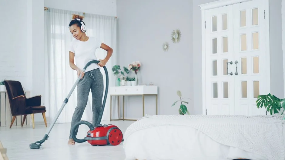 A person in personal protective equipment vacuuming indoors, ensuring a thorough clean.